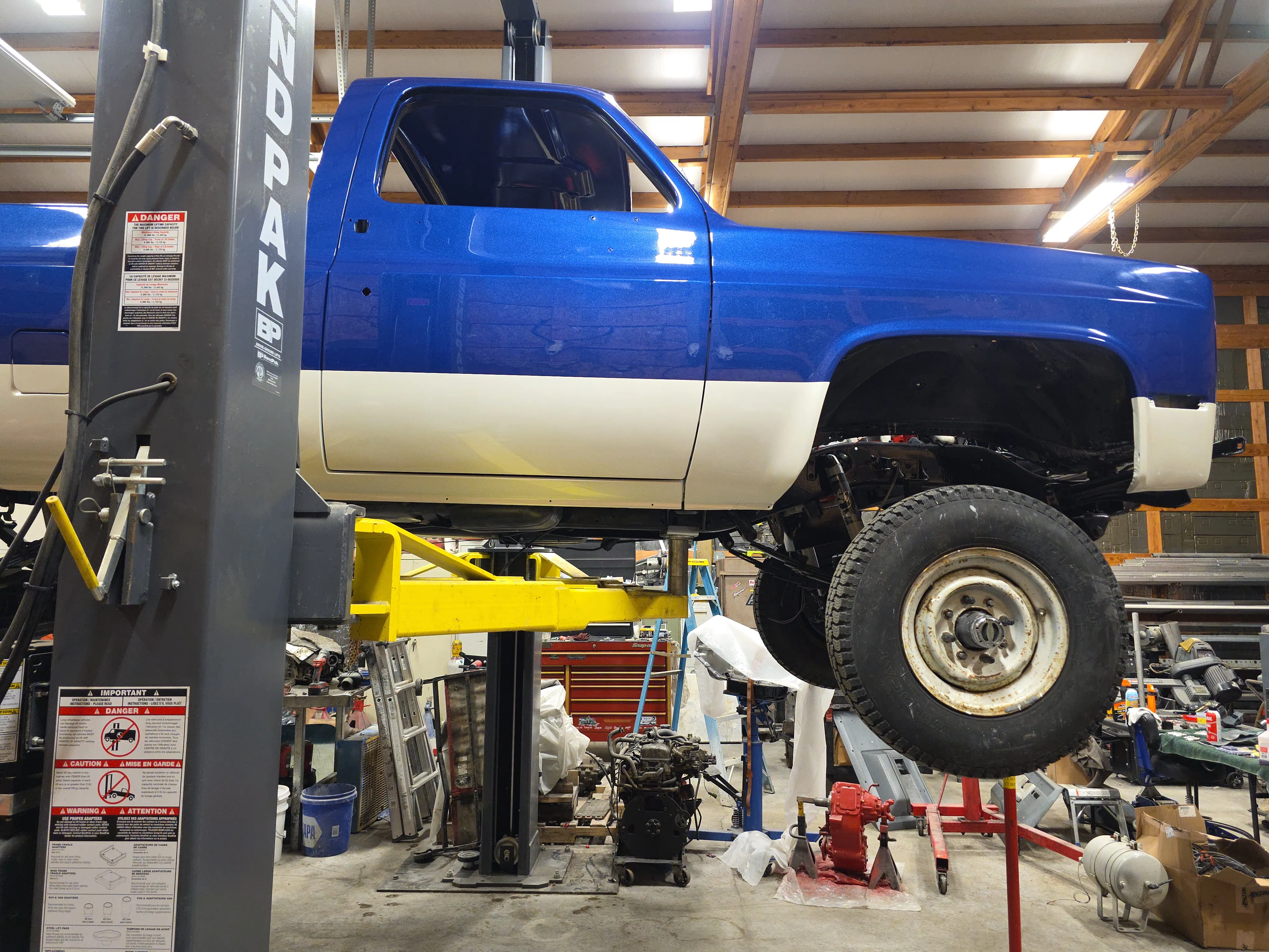 A custom blue squarebody pickup raised on a two-post lift in the shop